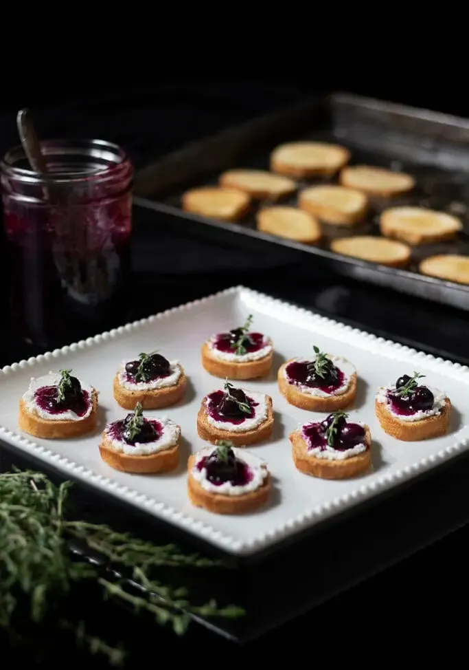prato de aperitivos ao lado de um pote de compota de mirtilo.' title=