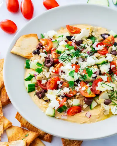 Lanches da Dieta Mediterrânea: molho de hummus em uma tigela com coberturas vegetarianas e chips de pão sírio.