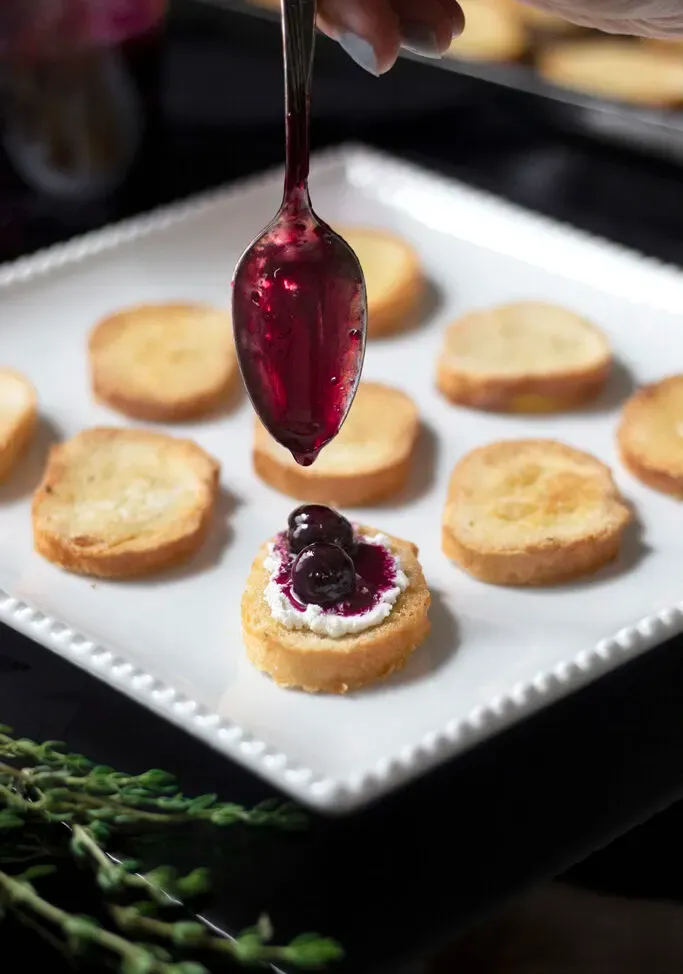 une cuillère déposant la compote de myrtilles sur une petite tartine.' loading='lazy' title=