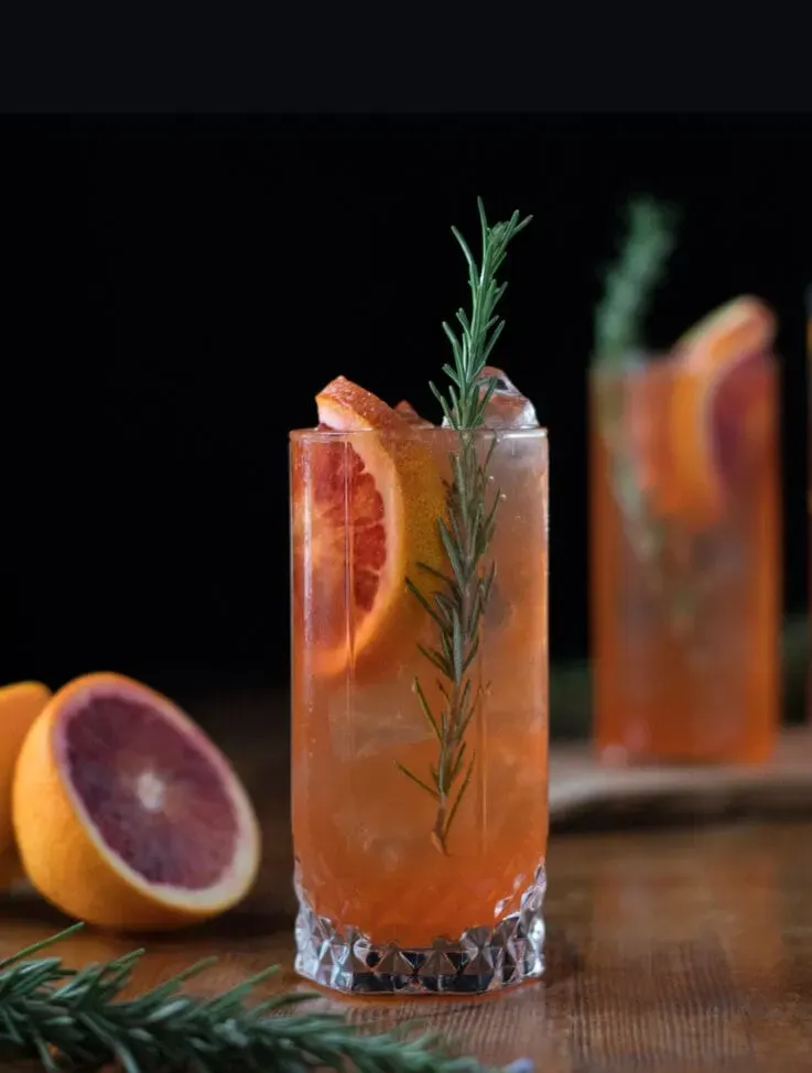 dva highball poháre naplnené pomarančovým nápojom a plátkami krvavého pomaranča.' title=