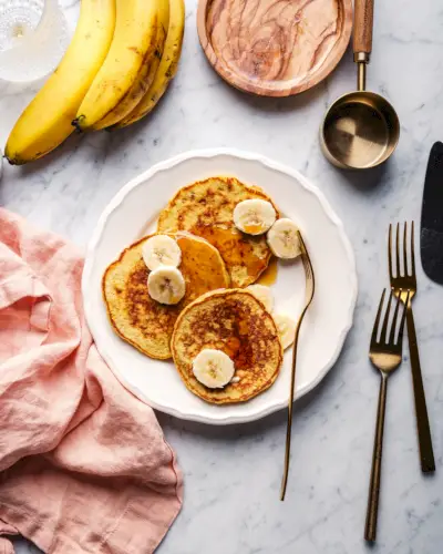 Panquecas de banana com 3 ingredientes com cacho de bananas, preparação para o café da manhã e guardanapos.