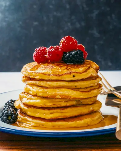Crêpes au fromage cottage en pile avec des baies et du sirop d'érable.