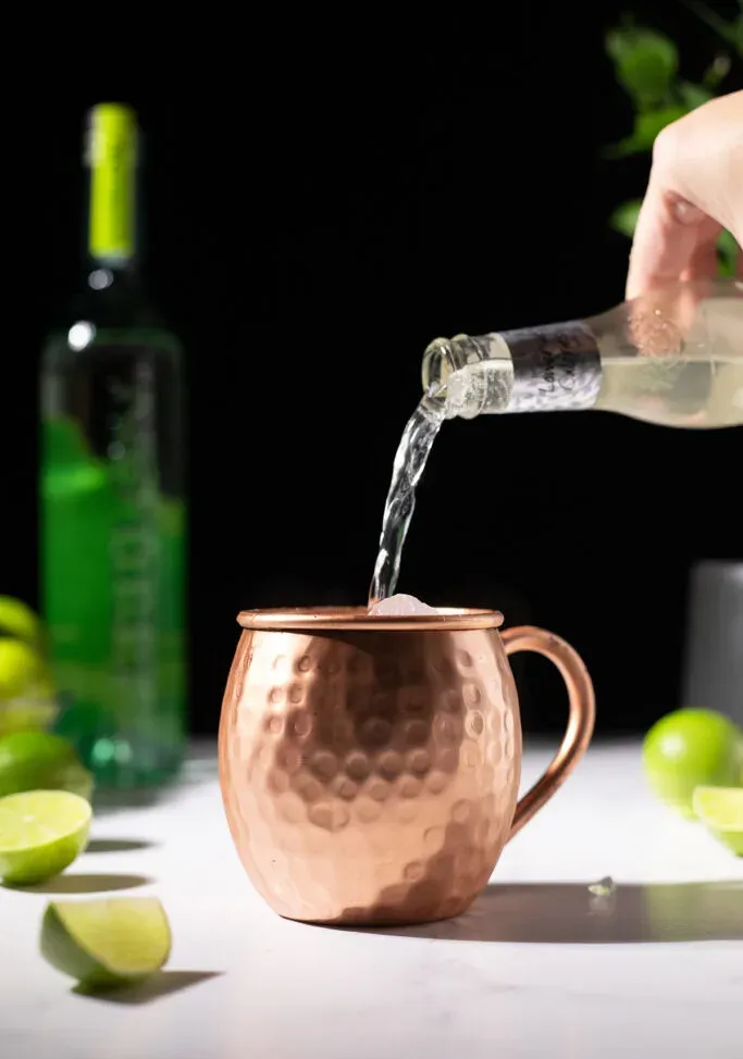 versando la birra allo zenzero Fever-Tree in una tazza di rame piena di ghiaccio.' title=