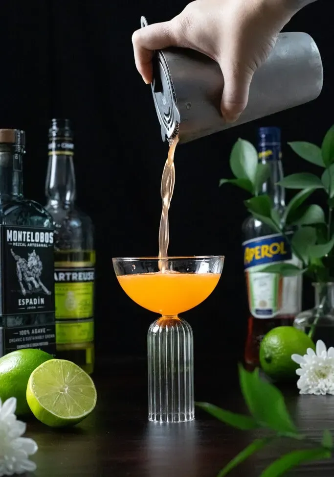 filtrer un cocktail à l'orange dans un verre coupé.' title=