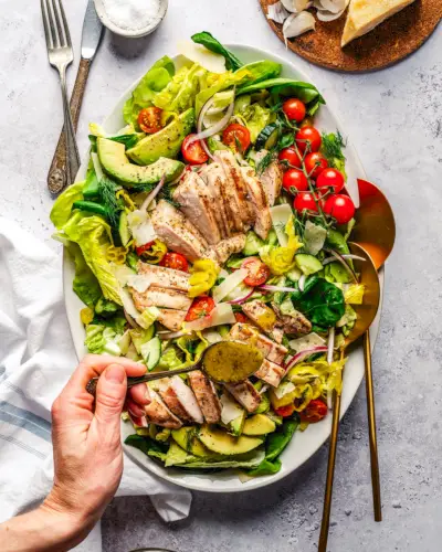 Recette de salade de poulet grillé sur assiette avec vinaigrette arrosée à la main.