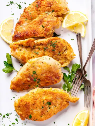 Poitrine de poulet en croûte de parmesan sur une assiette avec des quartiers de citron