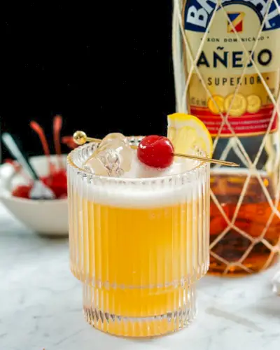 Cocktail azedo de rum com garrafa de rum escuro.