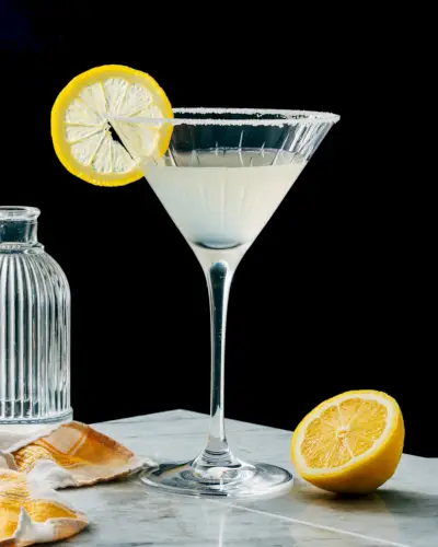 Martini com gota de limão em taça de martini com guarnição de limão e borda de açúcar.