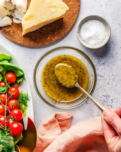 Italienisches Dressing in einer Schüssel mit Löffel, Salat und Parmesankäse.