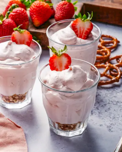 Rezept für Erdbeermousse in Tassen mit Erdbeeren und Brezeln im Hintergrund.