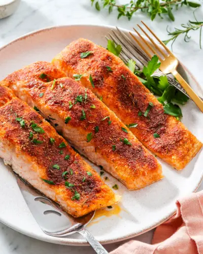Im Ofen gebackener Lachs auf einem Teller mit Serviergabeln und garniert mit Petersilie.
