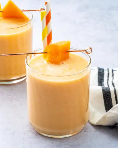 Smoothie de melão com pedaço de melão e dois canudos