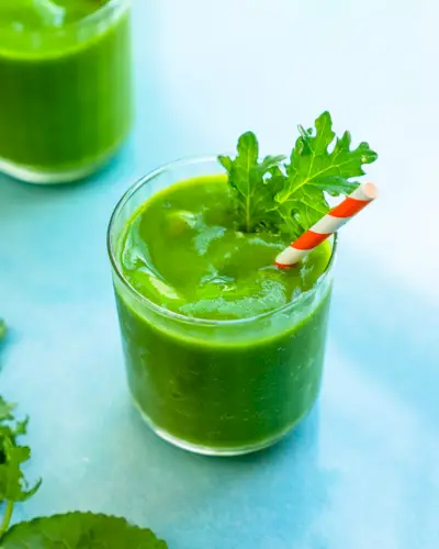 Smoothie au chou frisé dans un verre avec garniture de paille et de feuilles de chou frisé.