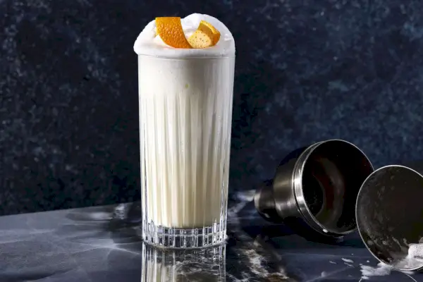 Ramos Gin Fiz in einem Collins-Glas mit orangefarbener Note vor grauem Hintergrund
