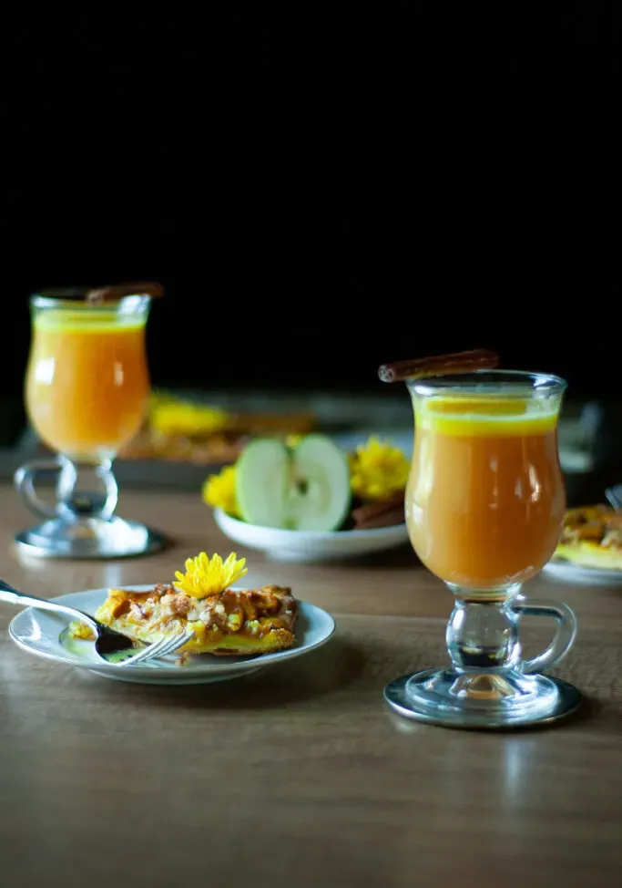 zwei Gläser scharfer Butterrum mit Kurkuma-Chai und einer Scheibe Apfelkuchen.' loading='lazy' title=