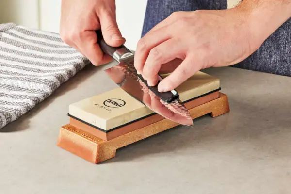 ידיים משחיזות סכין באמצעות סט המתנע של King Whetstone המונח על דלפק