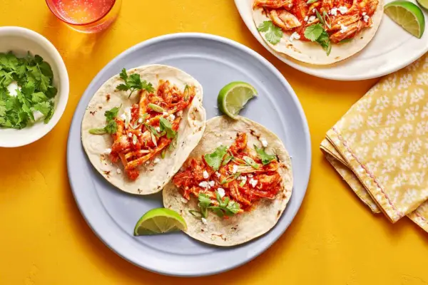 Talíř se dvěma kuřecími tacos tinga podávanými s plátky limetky, koriandrem a queso fresca