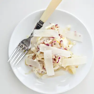 Pohľad zhora na feniklový a červený cibuľový šalát s parmezánom podávaný na bielom tanieri.