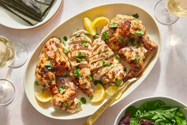 Un piatto di fette di pollo grigliato marinato nello yogurt, servito con spicchi di limone e insalata verde