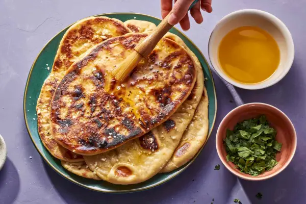 Un pincel que agrega mantequilla derretida a una pila de pan naan con ajo