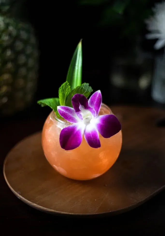 cocktail orange garni d'une orchidée violette.' title=