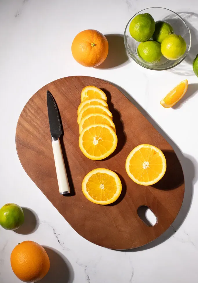 Schneidebrett mit einem Messer und einer in Scheiben geschnittenen Orange' title=