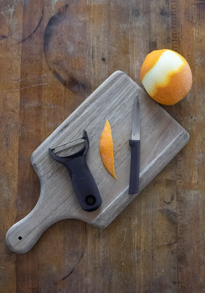 tábua de corte com casca de laranja, descascador de vegetais de laranja e uma faca' title=