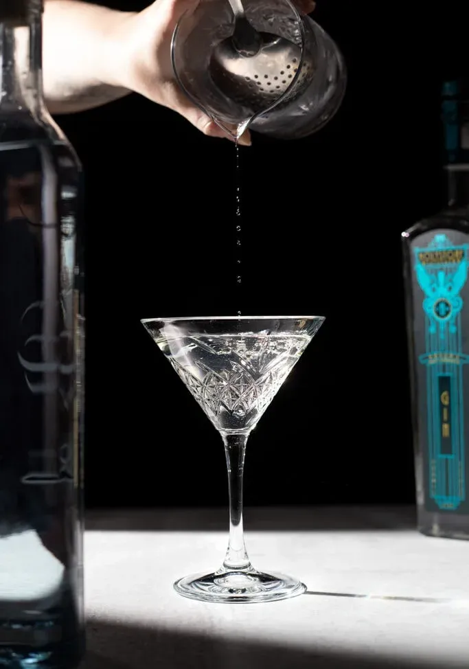 versare le ultime gocce di un cocktail dal mixing glass alla coppetta martini' title=