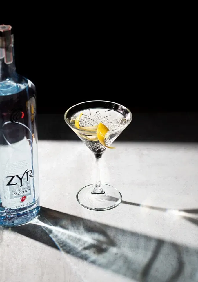 un martini con scorza di limone accanto a una bottiglia di vodka Zyr.' title=