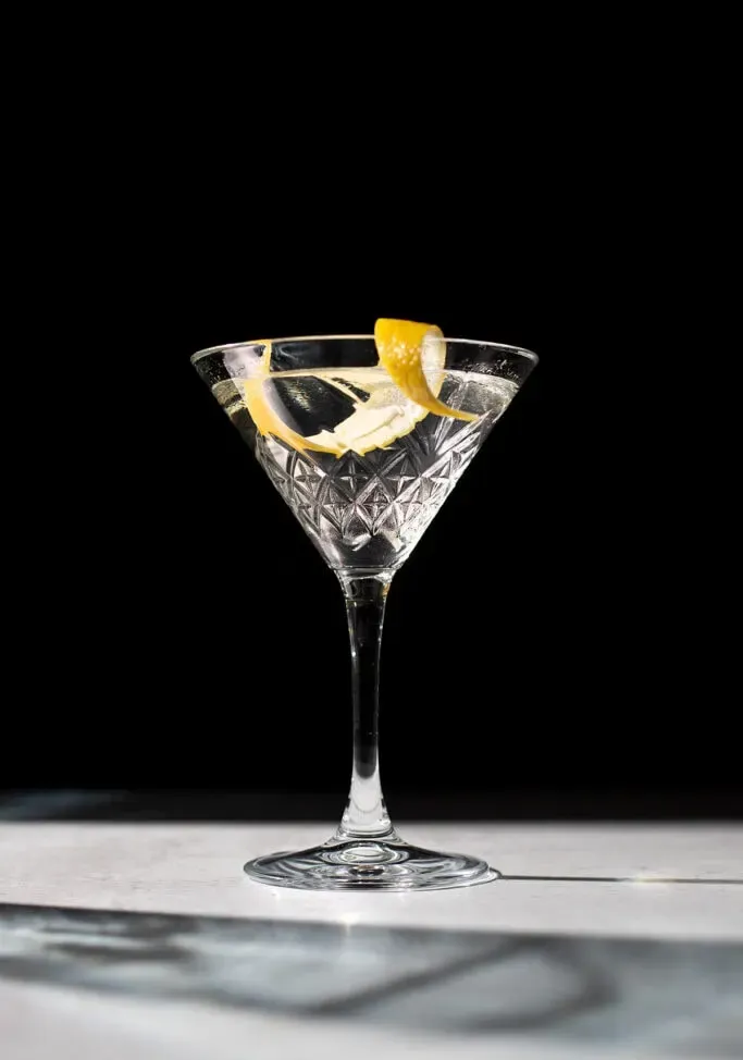 un martini con una scorza di limone su sfondo nero.' title=