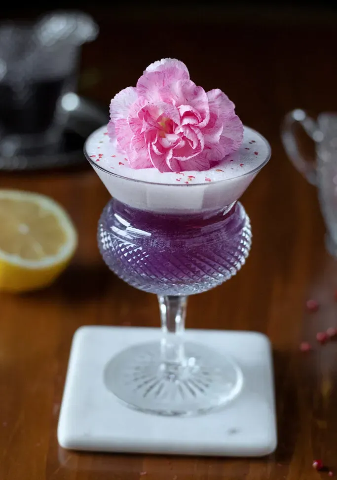 close-up de coquetel roxo com enfeite de flor rosa.' loading='lazy' title=