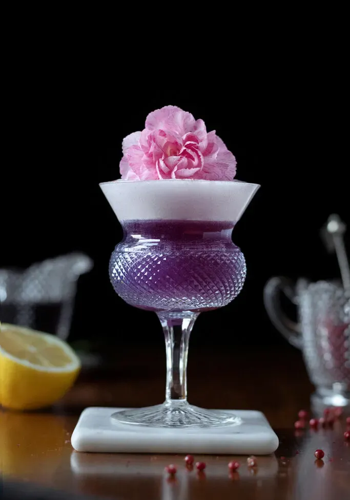 coquetel roxo com enfeite de flor rosa e meio limão.' title=