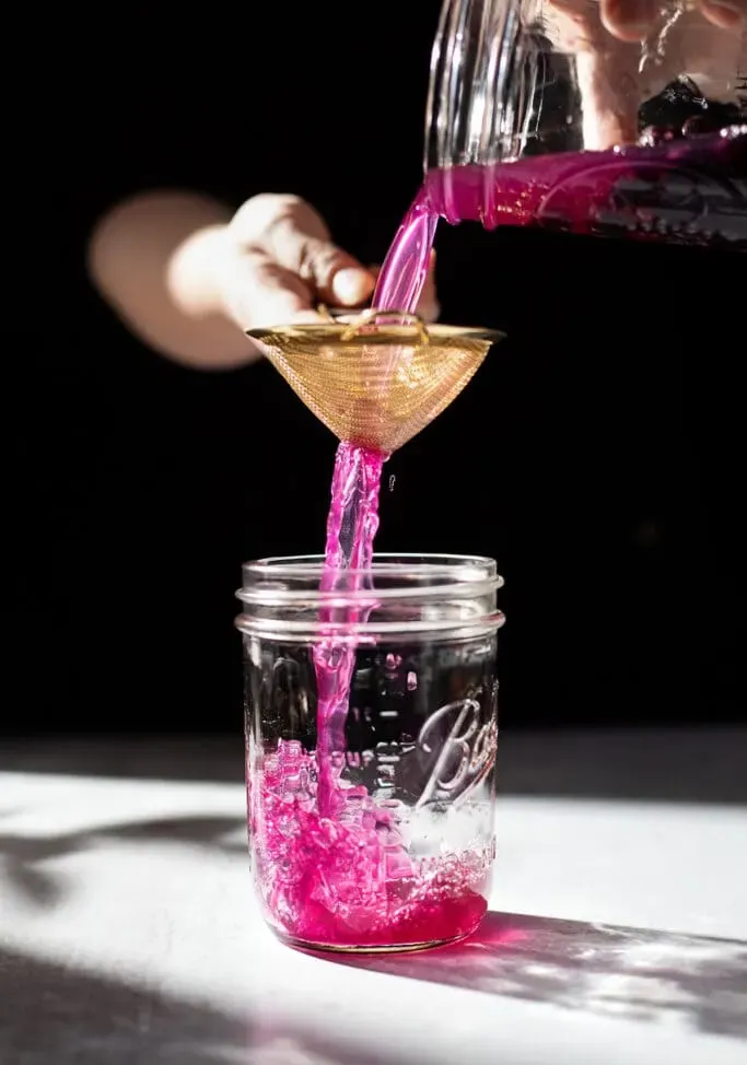 미세한 망사 여과기를 통해 메이슨 병에 붓는 분홍색 액체' loading='lazy' title=