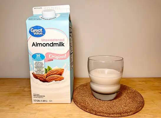 a container of great value almond milk next to a glass of it