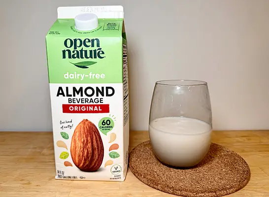 a container of open nature almond milk next to a glass of it