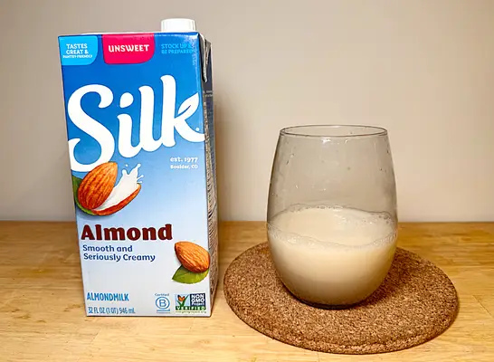 a container of silk almond milk next to a glass of it