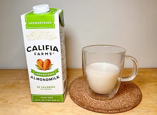 a container of califia almond milk next to a glass of almond milk