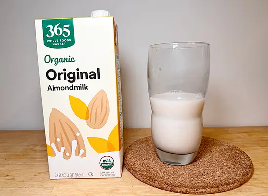 a container of 365 almond milk next to a glass of it