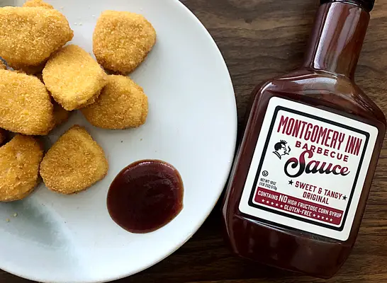 a bottle of montgomery inn bbq sauce next to a plate of chicken nuggets
