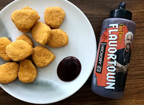 a bottle of guy fieri bbq sauce next to a plate of chicken nuggets