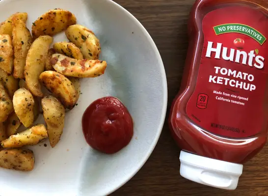 hunts ketchup bottle with ketchup and fries on a plate.