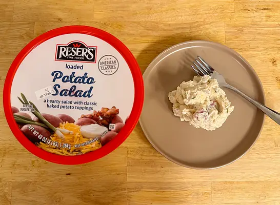 a container of loaded potato salad next to a dish of potato salad