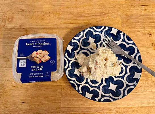 a container of bowl and basket potato salad next to a dish of potato salad