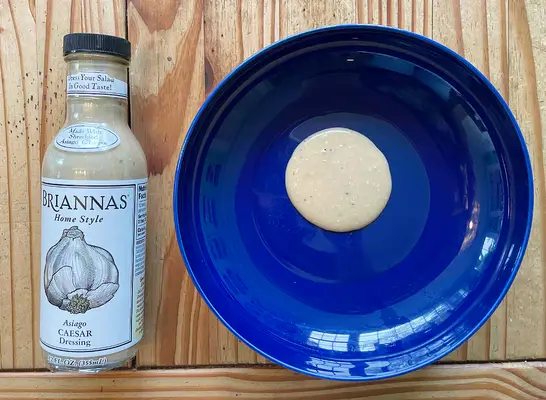 a bottle of caesar dressing next to a blue plate with dressing on it.