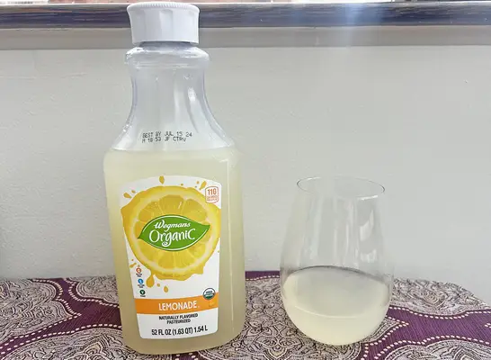 A bottle of Wegmans private-label lemonade next to a small glass of the beverage.
