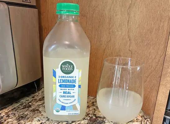 A bottle of Whole Foods private-label lemonade next to a small glass of the beverage.