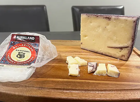 a block of kirkland bellavitano cabernet cheese on a cutting board with the wrapper next to it