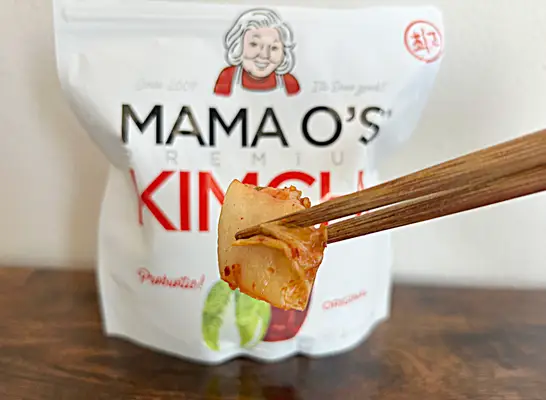 a bag of mama o kimchi with chopsticks holding kimchi