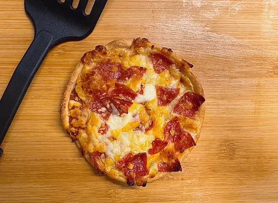 a single pepperoni pizza on a cutting board with a black spatula.