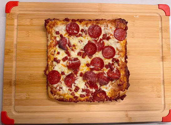 a square pepperoni pizza on a cutting board.
